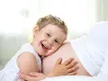 Bambina di 3 anni felice abbraccia la pancia della mamma, in attesa dell'arrivo di un fratellino.