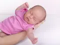 Neonato in rosa si irrigidisce e stringe i pugni, dormendo sereno tra le braccia.