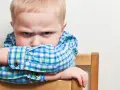 Bambino di 20 mesi ingestibile, con sguardo corrucciato e braccia incrociate sulla sedia.