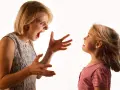 Una madre sgrida il figlio con veemenza, le mani aperte in un gesto di rimprovero. La bambina la guarda, visibilmente scossa.