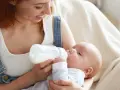 Mamma con capelli rossi nutre il suo neonato con latte artificiale ogni 2 ore. Il piccolo beve con gusto dalla bottiglia.