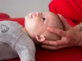 Un neonato sbatte la testa sul petto, con mani adulte che lo sostengono delicatamente.
