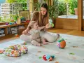 Mamma gioca con un neonato di 6 mesi che non sta seduto, su un tappeto gioco con tanti giocattoli colorati.