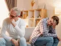 Padre e figlio seduti sul divano, distanti e pensierosi. Crescere in una famiglia dove si litiga sempre lascia segni profondi.