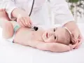 Un neonato sorride mentre il pediatra ascolta il suo respiro con uno stetoscopio.