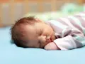 Un neonato dorme sereno, ma chissà se i neonati sognano incubi. La sua manina è vicino alla bocca, il pigiamino a righe lo avvolge.