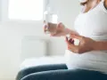 Donna incinta tiene una pillola e un bicchiere d'acqua. L'uso di cortisone in gravidanza va valutato attentamente.