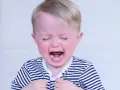 Bambino di 2 anni con capelli biondi, occhi chiusi e bocca spalancata in un pianto disperato, tipico dei capricci continui. Indossa una maglietta a righe.