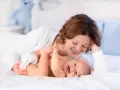 Mamma sorride mentre gioca con il suo neonato, svegliandolo dolcemente per mangiare.