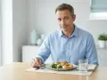 Uomo con piatto di pollo e patate, sguardo incerto, forse con paura di mangiare.