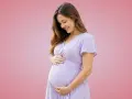 Donna incinta sorride, accarezzando il pancione. Importante assumere acido folico prima o dopo i pasti per la salute del bambino.