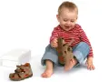 Bambino di 18 mesi, con un comportamento curioso, gioca con un sandalo marrone.