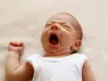 Un neonato sbadiglia profondamente, con gli occhi chiusi e la bocca spalancata, un momento di pura stanchezza prima di nuove finestre di veglia.