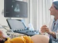 Ecografia di una donna incinta, con il medico che usa la sonda per sentire il battito del feto. L'emozione sul volto della futura mamma è palpabile.