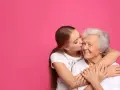 Una ragazza bacia la guancia della nonna, abbracciandola. Si vede che i figli assomigliano ai nonni, un legame d'amore.