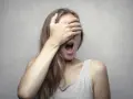 Ragazza con la mano sugli occhi, bocca spalancata, forse per la fobia del vomito (emetofobia).