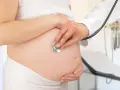 Visita medica per monitorare la gravidanza. Il medico ascolta il battito cardiaco del feto con uno stetoscopio sul pancione.