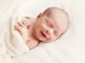 Un adorabile neonato non dorme, ma sorride beatamente avvolto in una coperta morbida.