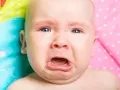 Un neonato piange dopo poppata, con gli occhi azzurri spalancati e la bocca aperta in un lamento.