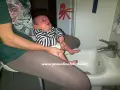 Un bimbo fa pipì in giro mentre è seduto sul lavandino, con un adesivo di polpo sul muro.