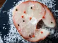 Raw swordfish steak with salt and peppercorns on a dark slate.