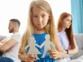 Bambina con sagome di carta di una coppia, mentre i genitori separati sono sullo sfondo.