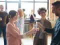 Persone brindano con drink, i loro occhi che si incrociano trasmettono un'ansia sottile, ma anche speranza.