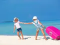 Due bambine con valigia rosa su spiaggia tropicale: idee per cosa fare a Ferragosto con i bambini.