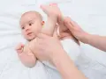 Mani che aiutano un neonato a liberarsi dall'aria nella pancia, con le gambine sollevate delicatamente.