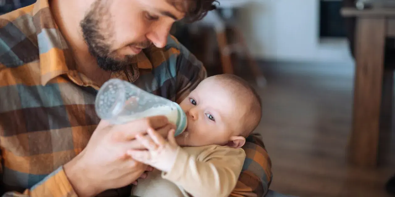 Padre con barba nutre il neonato con il biberon. Scopri trucchi per far prendere il biberon al tuo piccolo.