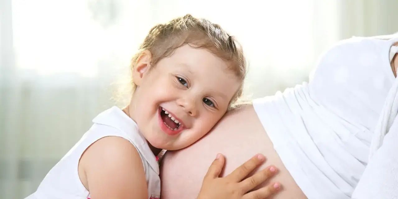 Bambina di 3 anni felice abbraccia la pancia della mamma, in attesa dell'arrivo di un fratellino.
