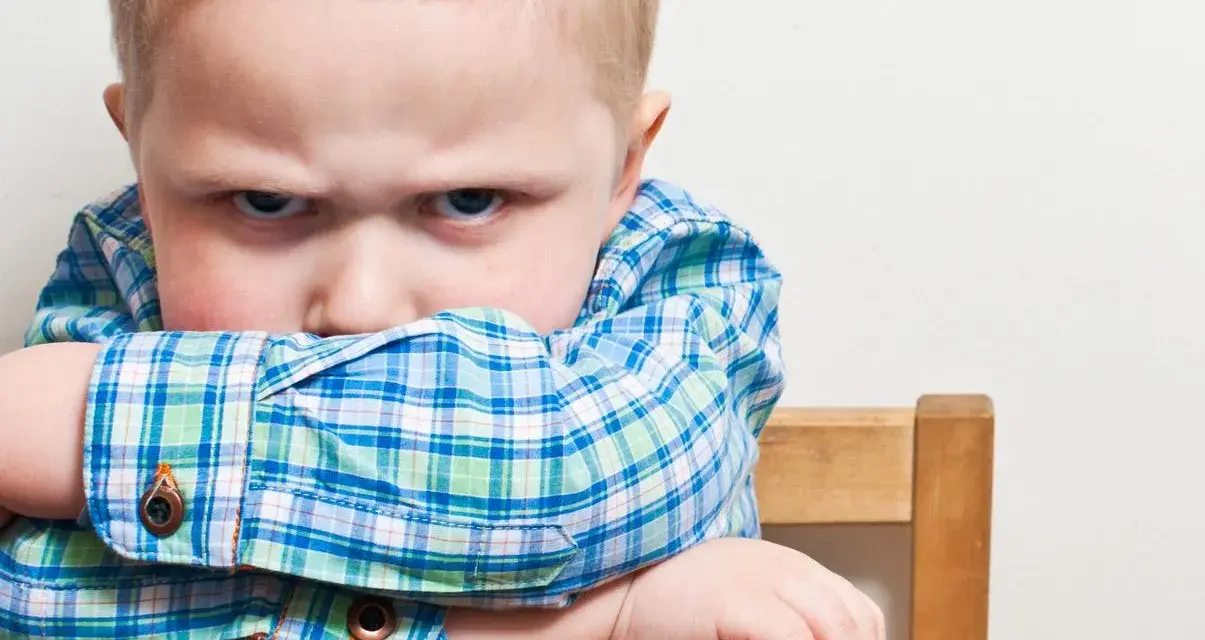 Bambino di 20 mesi ingestibile, con sguardo corrucciato e braccia incrociate sulla sedia.
