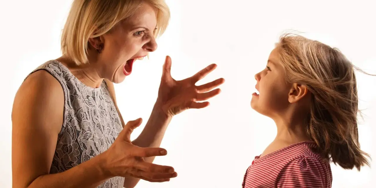 Una madre sgrida il figlio con veemenza, le mani aperte in un gesto di rimprovero. La bambina la guarda, visibilmente scossa.