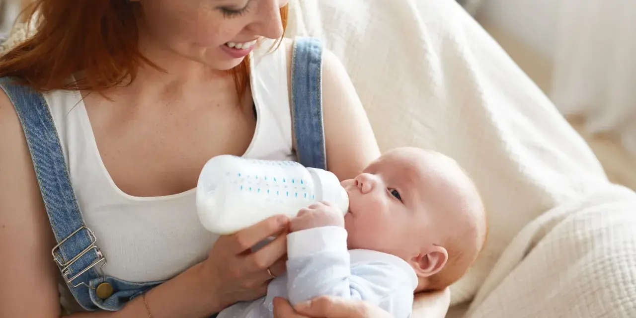 Mamma con capelli rossi nutre il suo neonato con latte artificiale ogni 2 ore. Il piccolo beve con gusto dalla bottiglia.