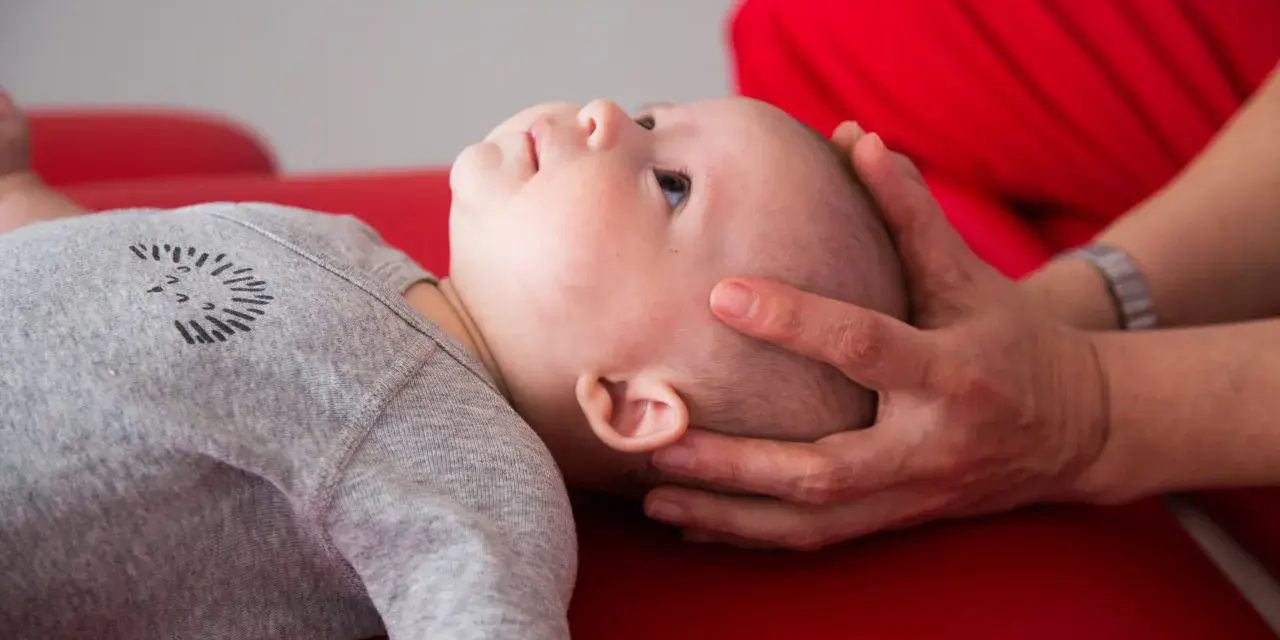 Un neonato sbatte la testa sul petto, con mani adulte che lo sostengono delicatamente.