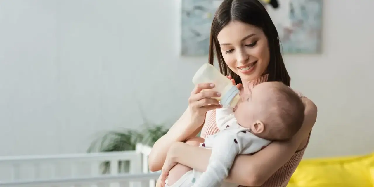 Mamma sorridente nutre il neonato con latte artificiale. Il piccolo potrebbe avere cacca liquida, ma ora è felice.