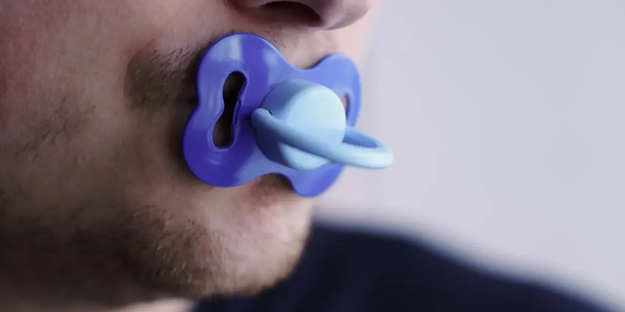 Un uomo con barba corta ha un ciuccio blu in bocca, un'immagine che evoca adulti che si comportano da bambini.