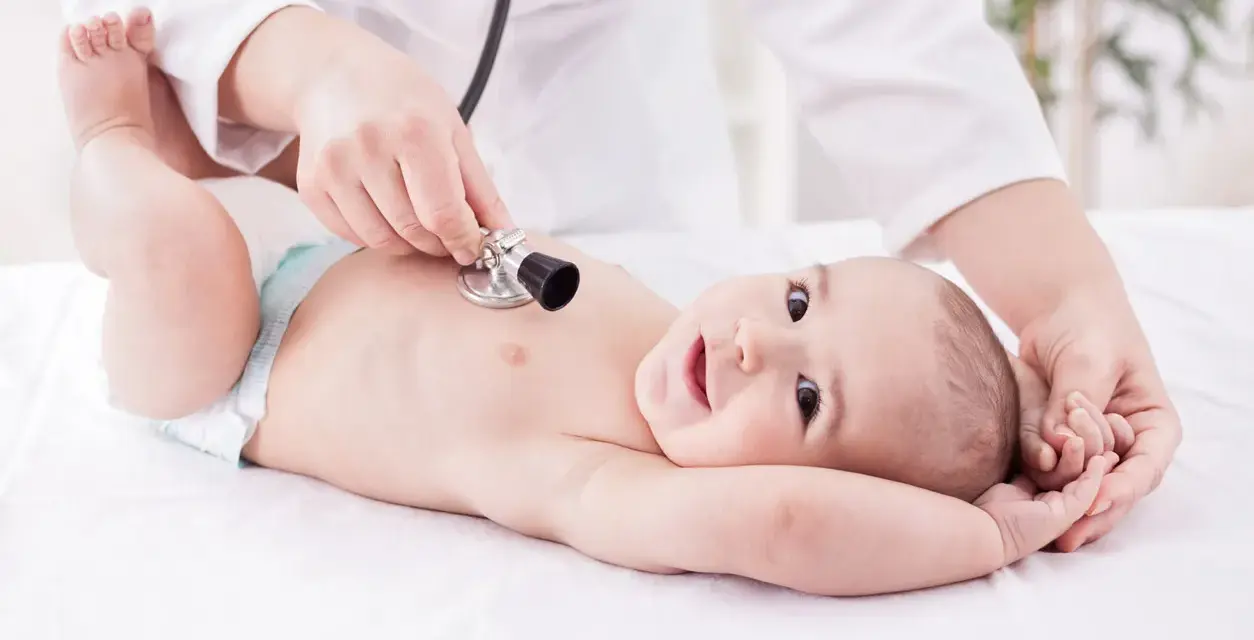 Un neonato sorride mentre il pediatra ascolta il suo respiro con uno stetoscopio.