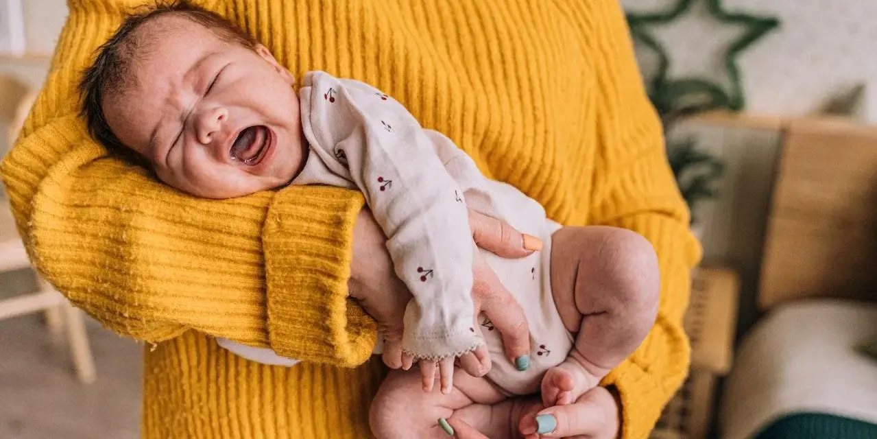 Neonato di 11 mesi con scatti nervosi, piange tra le braccia di chi lo tiene, avvolto in un maglione giallo.