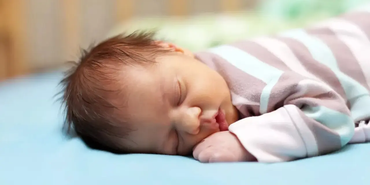 Un neonato dorme sereno, ma chissà se i neonati sognano incubi. La sua manina è vicino alla bocca, il pigiamino a righe lo avvolge.