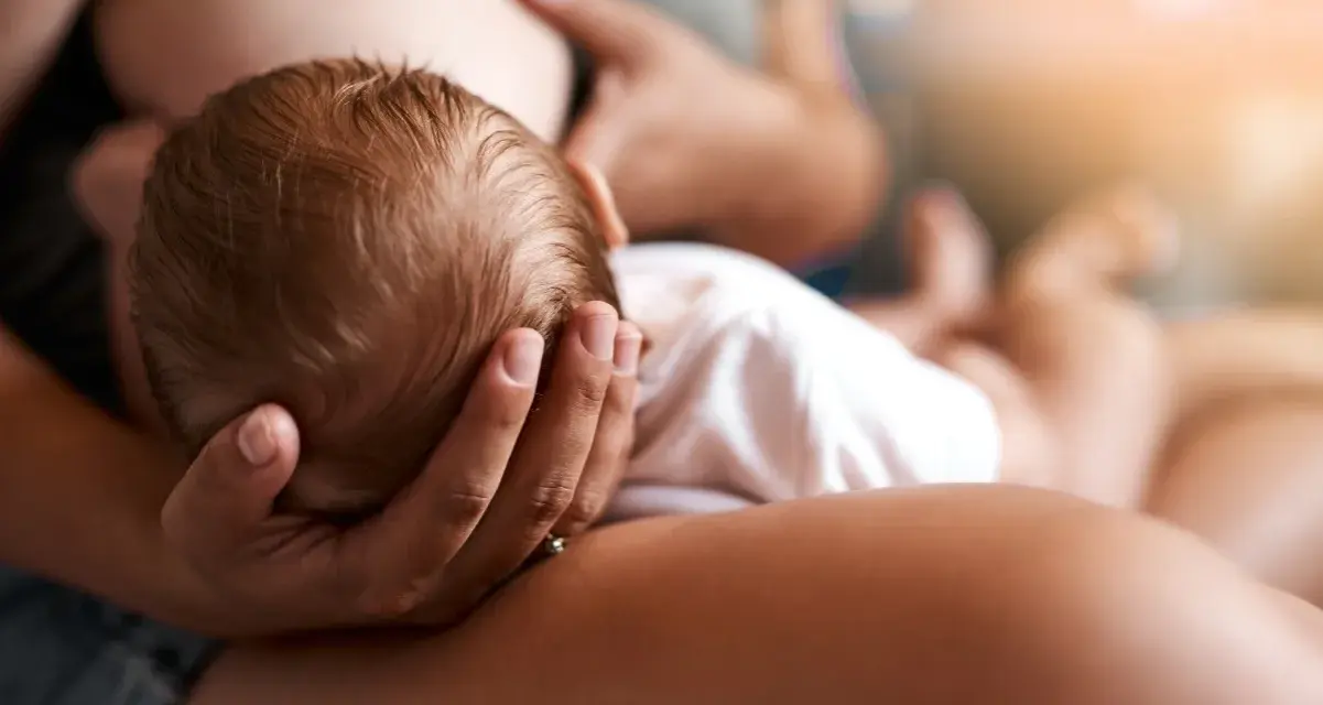 Un neonato si nutre al seno, la sua testolina è tenuta da una mano. La montata lattea non arriva, ma l'amore è presente.