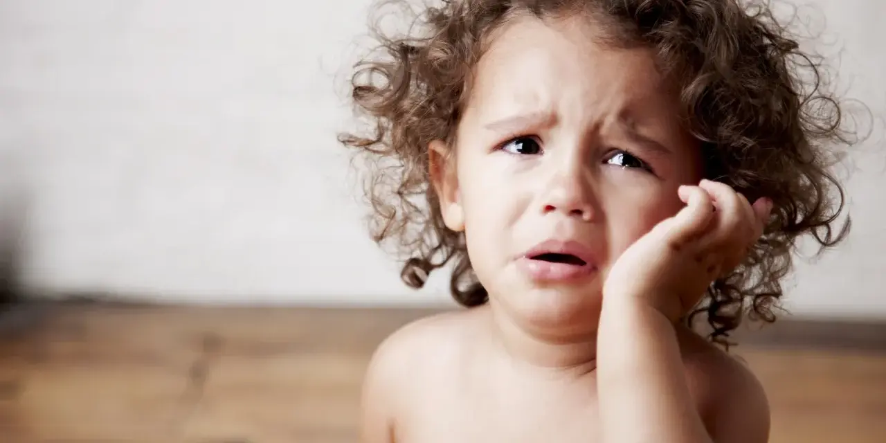 Bambino con riccioli castani piange, forse è un modo per comunicare il disagio, ecco perchè i bambini mordono.