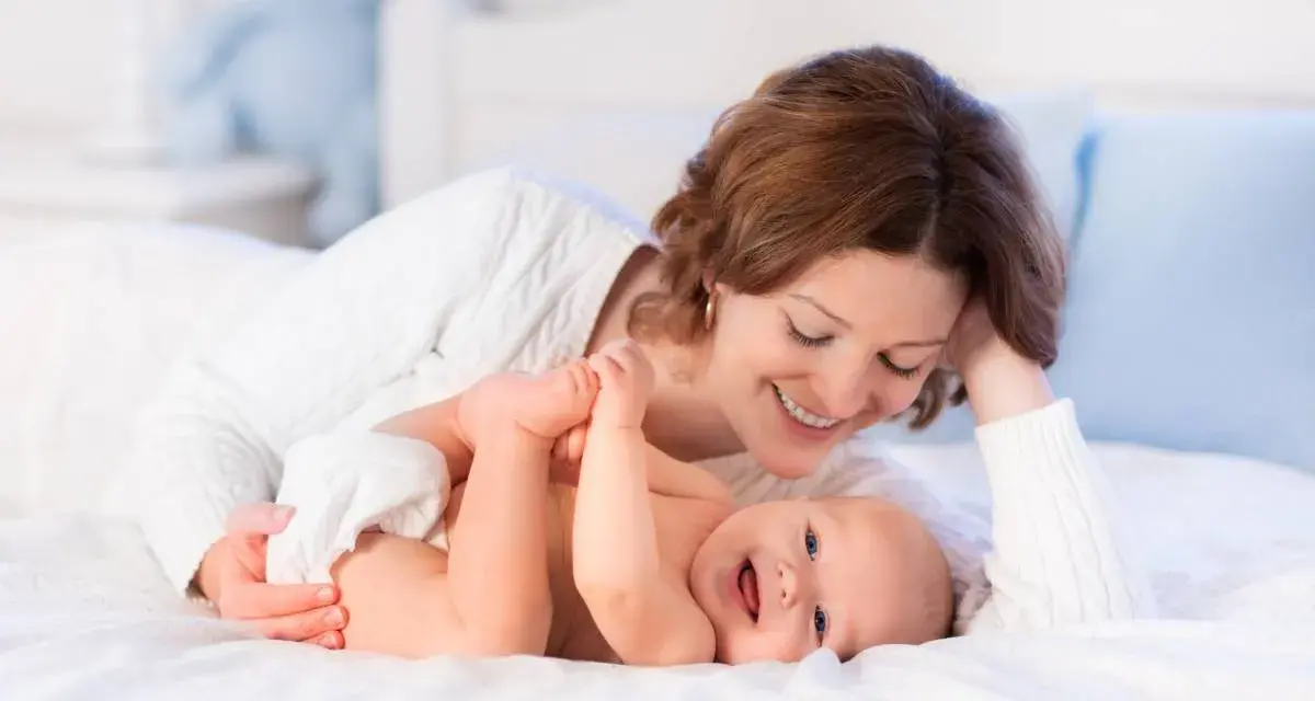 Mamma sorride mentre gioca con il suo neonato, svegliandolo dolcemente per mangiare.