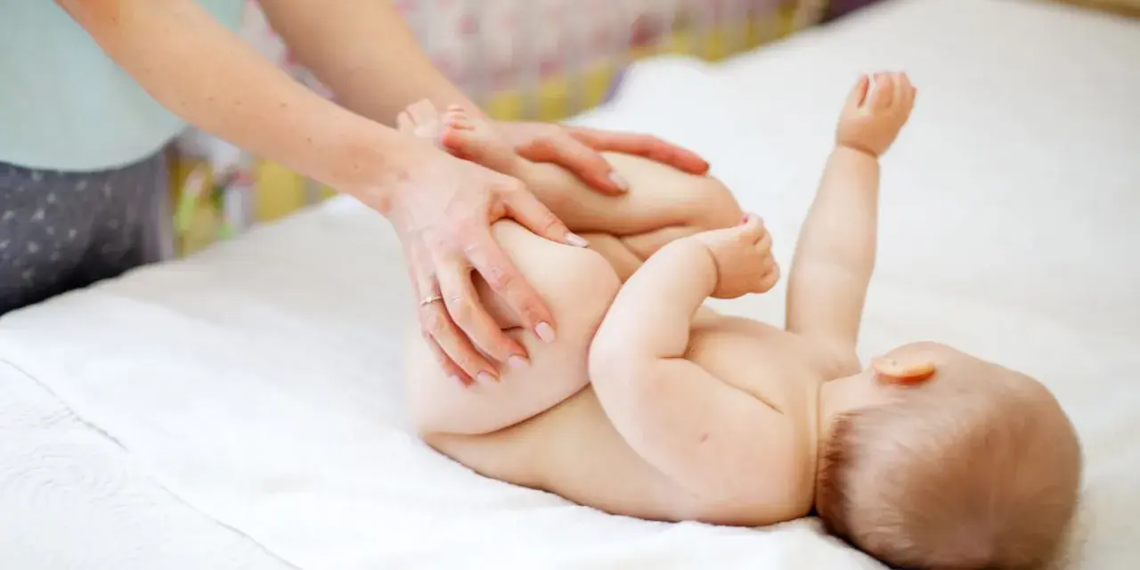 Mani che aiutano il neonato a fare la cacca con movimenti delicati sulle gambine.