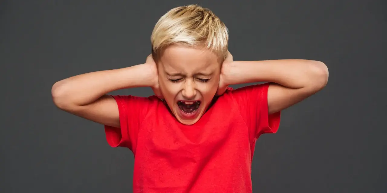 Bambino di 7 anni in crisi di rabbia, urla coprendosi le orecchie.