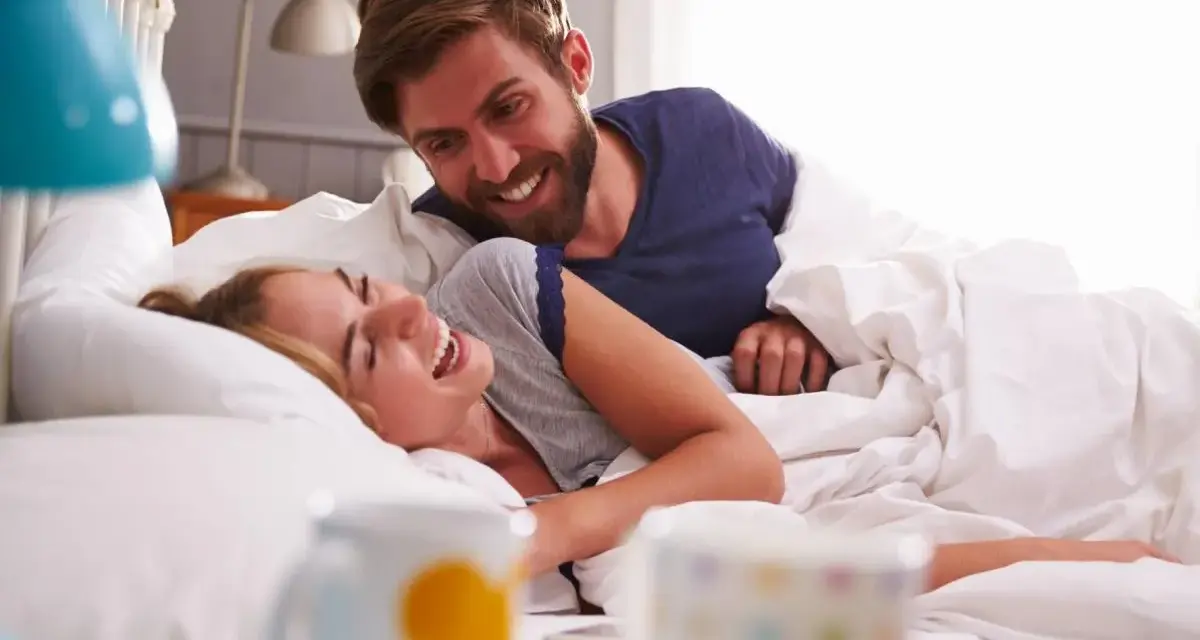 Coppia sorridente a letto, un momento di gioia che va oltre i rapporti promiscui, un legame profondo.
