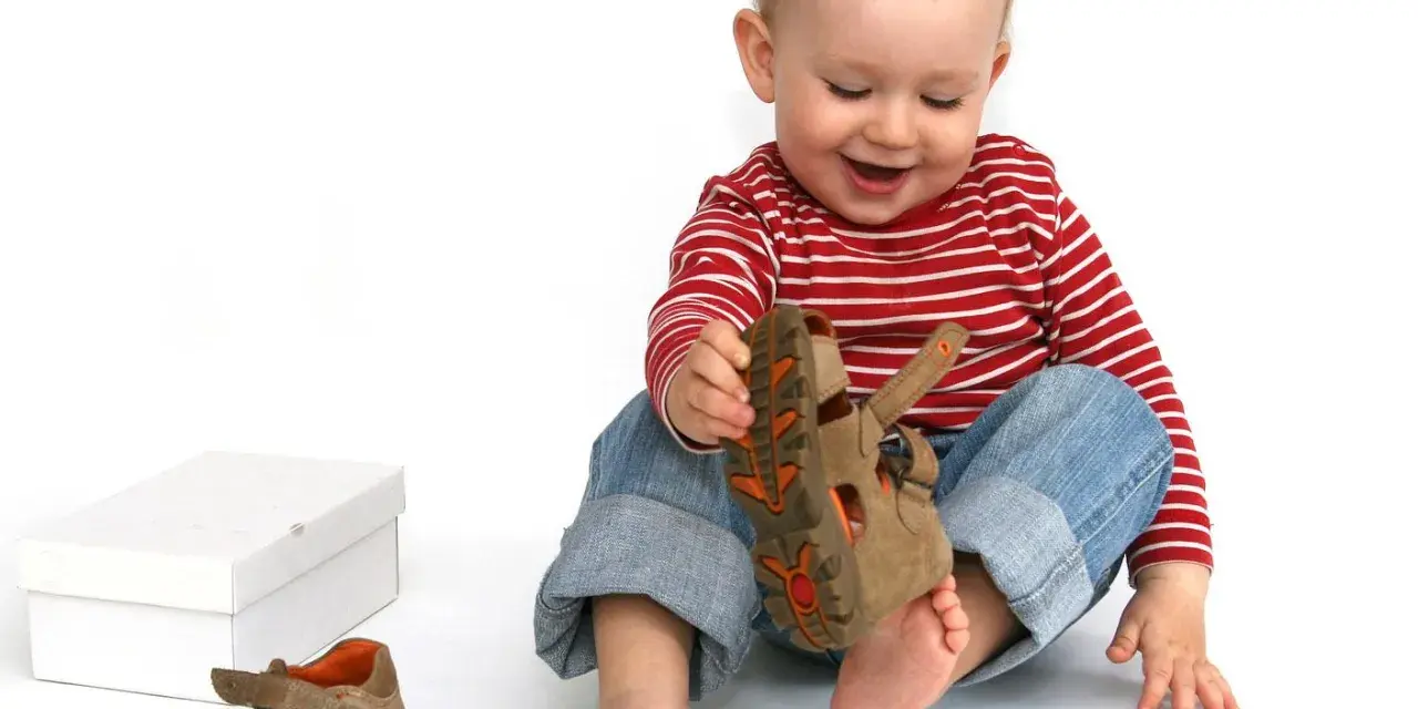 Bambino di 18 mesi, con un comportamento curioso, gioca con un sandalo marrone.