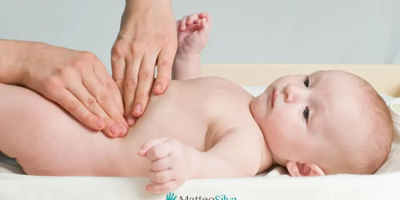 Mani che massaggiano la pancia di un neonato, forse per alleviare coliche o cacca acida. Un momento di cura per i più piccoli.