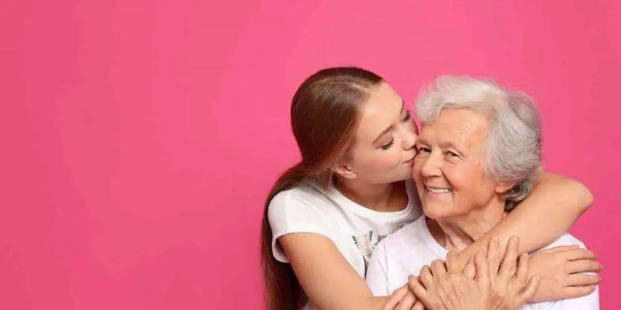 Una ragazza bacia la guancia della nonna, abbracciandola. Si vede che i figli assomigliano ai nonni, un legame d'amore.