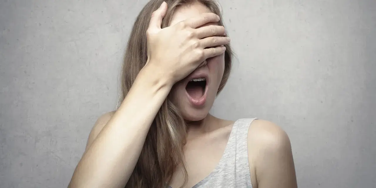 Ragazza con la mano sugli occhi, bocca spalancata, forse per la fobia del vomito (emetofobia).